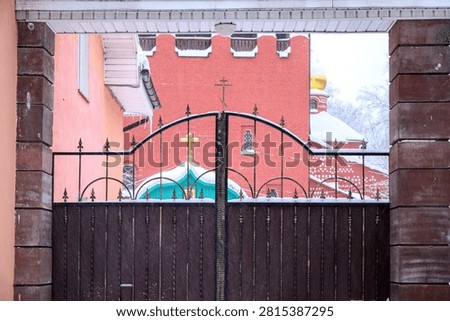 A view through a framed gate with an arched top and dark slats, revealing a vibrant red brick Orthodox church with a gold cross and a turquoise roof