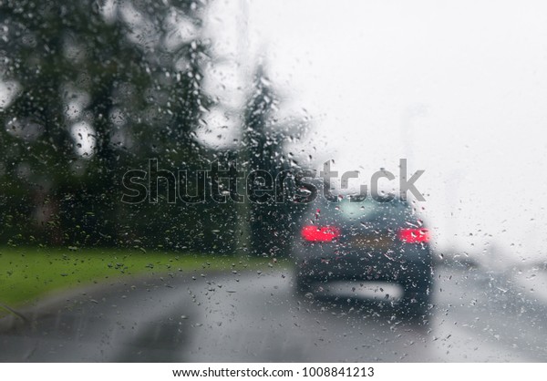 View through glass\
with raindrops of a car traveling along a wet road on a rainy day. \
Image taken in the UK.