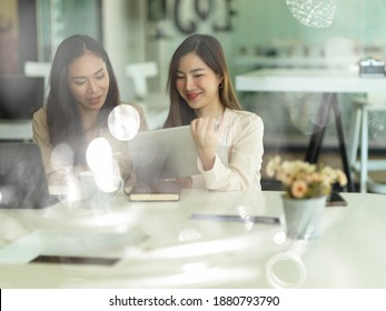 View Through Glass Wall Of Two Businesswomen Talking To Each Other While Working In Office Room