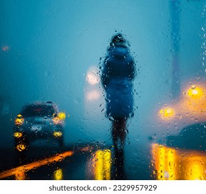 View through glass window with rain drops on blurred  silhouette of a girl on a city street after rain and colorful neon bokeh city lights, night street scene. Focus on raindrops on glass - Powered by Shutterstock