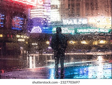 View through a glass window with raindrops on a blurred silhouette of a man  with umbrella walking on autumn rain , night street scene. focus on raindrops - Powered by Shutterstock