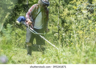 View Through High Grass Of A Man With Protective Head-wear And Goggles Trimming The Lawn With Weed Eater.