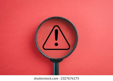 View through a magnifying glass on Exclamation mark or Warning sign over red background Attention sign,Exclamation mark,warning sign concept.
