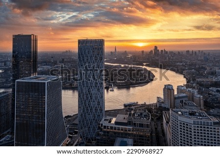 View through the modern skyscrapers of Canary Wharf of the urban London skyline and Thames river during sunset time, England
