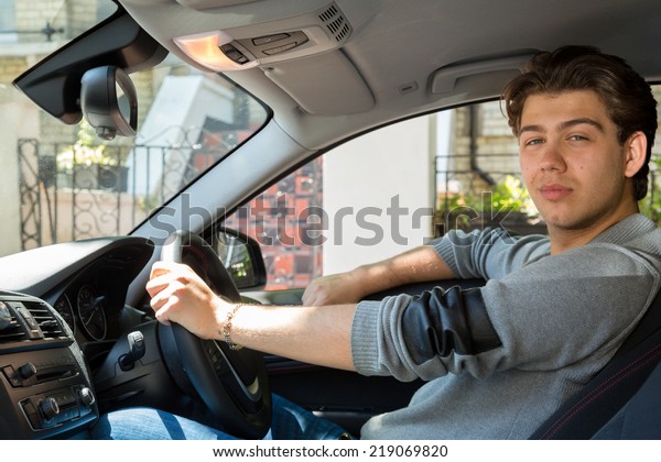 View through the open\
passenger window of a young man driving his car in town turning to\
look at the camera