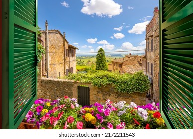 View through an open window with shutters and a flowerbox out over the Tuscan countryside and medieval hilltop old town of San Gimignano, Italy.