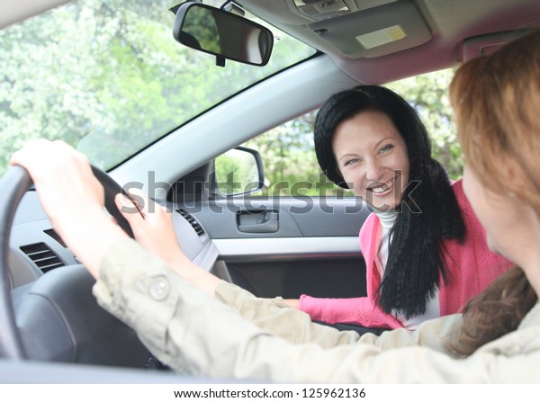 View through past\
the female driver to an attractive woman passenger in a motor car\
with focus to the\
passenger