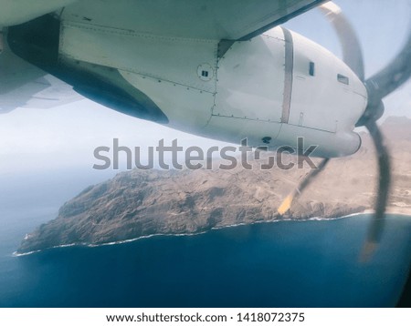 View through a plane window of the engine and propellers above the ocean and island