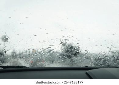 View through a rain-covered windshield from inside a car, capturing the blurry scenery and mood of a rainy day on the road.