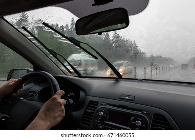View through the rain-drenched windshield. Blurred silhouettes of vehicles. Driver's hands and part of the car interior