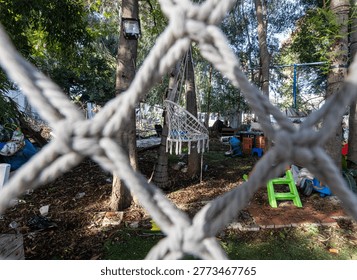 View through rope net into messy backyard with chair and objects, concept of barrier, restriction or hidden space.