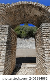 View through a round arch of the proscenium of the Hellenistic theatre remains dated in the mid-III c.BC due to the dedicatory inscription in the parodos, Butrint archaeological site. Sarande-Albania.
