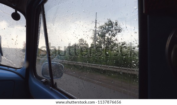 View\
through the side window of the old retro car while moving at rainy\
weather. Raindrops falling on the glass of vintage automobile\
during drive at countryside. Close up Slow\
motion.