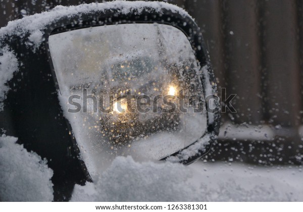 View through snow covered car mirror, coming car with\
lights on