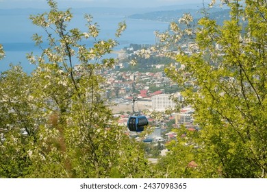 View through trees on cableway with moving funicular cabin and coastal Batumi city, Black sea from high mountains. Ropeway, cable car in Georgia. Travel, tourism, vacation, wanderlust concept.