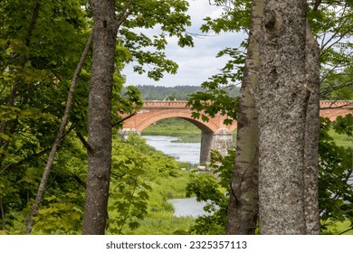 a view through the trees of a red bridge over a calm river