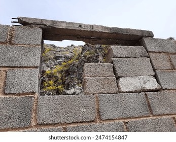 View through an unfinished cinder block wall in Lin, Albania, revealing rocky terrain with yellow wildflowers. The rough texture of the blocks contrasts with the natural landscape. Old and new collide - Powered by Shutterstock