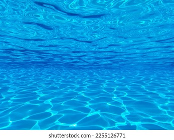 The view through a viewing port between floor, bottom and surface of luxury swimming pool and blue water with sun reflections at the resort 