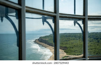 View through a window of a bronze statue in Montauk. A dark stone frame surrounds a glass window overlooking a monument near the ocean waves.