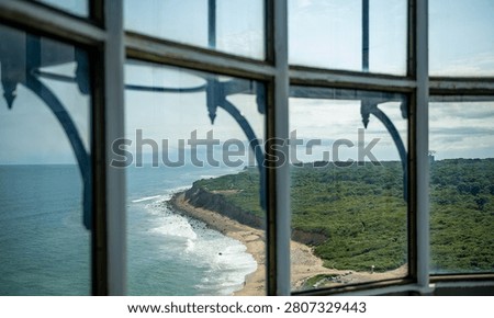 View through a window of a bronze statue in Montauk. A dark stone frame surrounds a glass window overlooking a monument near the ocean waves.