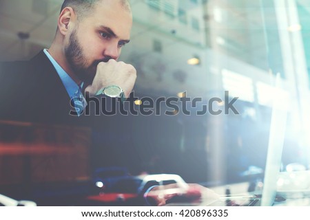 View through the window of a cafe with double exposition of young serious man successful trader is monitoring exchange trading via laptop computer, while is sitting in modern coffee shop interior