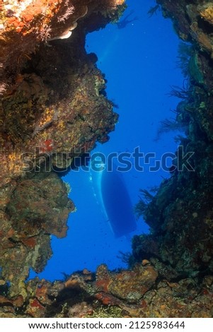 A view through a window of coral reef shows the hull of a dive boat bobbing around on the surface of the Caribbean sea fifty feet above.