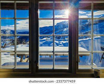 View through the window from cozy wooden cabin to snowy mountains during winter. Ski center accommodation. 