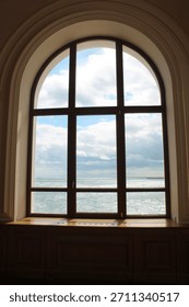 View through a window frame with multiple panes looking out at a large body of water under a cloudy blue sky. 