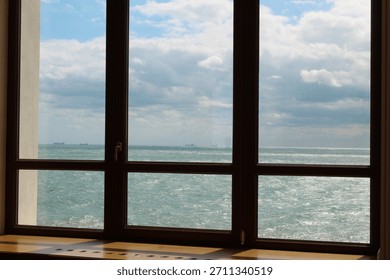 View through a window frame with multiple panes looking out at a large body of water under a cloudy blue sky. 