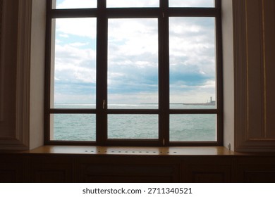 View through a window frame with multiple panes looking out at a large body of water under a cloudy blue sky. 