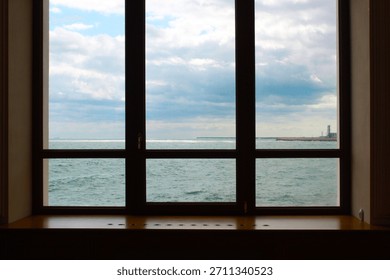 View through a window frame with multiple panes looking out at a large body of water under a cloudy blue sky. 