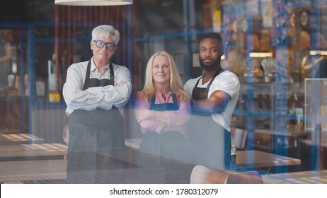 View Through Window Of Happy Diverse Waiters Looking At Camera With Hands Crossed In Restaurant. Successful Multiethnic Cafe Staff Smiling At Camera. Small Business And Teamwork Concept