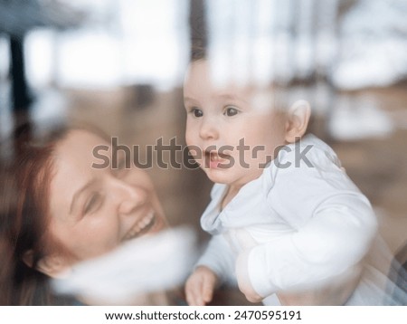 View through the window of a red-haired Caucasian woman holding her little son. 