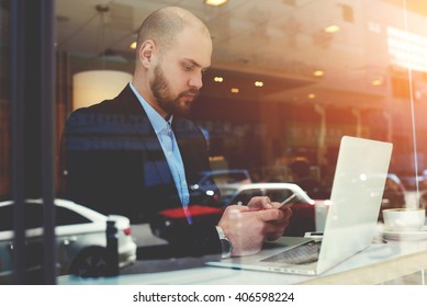 View Through Window With Reflection Street Of Confident Man Banker Is Typing Text Message On Mobile Phone, While Is Resting After Videoconferencing Via Laptop Computer During His Business Trip Abroad