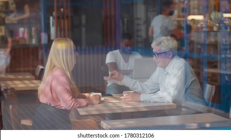 View through window of senior couple in love sitting in cafe talking and having fun. Happy retirement couple relaxing at coffee shop. Aged friends having coffee break in cafeteria - Powered by Shutterstock