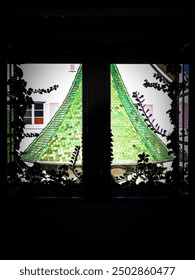 A view through a window showcasing a vibrant green roof adorned with plants. The window frame adds depth, while the lush greenery hints at a lively outdoor environment.
