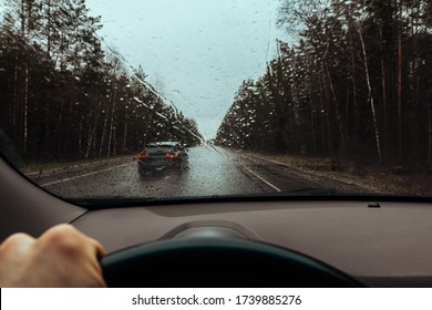 View through windshield of car on drops on glass, wet road and rainy weather. Highway car traffic in bad weather, downpour. Dangerous overtaking. Dashboard inside and driver hand with steering wheel