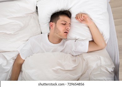 View Of Tired Young Man Snoring While Deep Sleeping In Bed