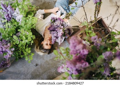 view top. an attractive blonde in a white shirt and jeans on the floor with lilac flowers. profession of a florist. fragrances and perfumes for the home. femininity and tenderness. feminine beauty. - Shutterstock ID 2184809427