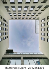 View to top to cloudy sky framed in walls of modern corporate building full of windows 