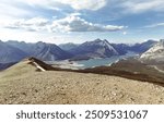 view from the top of a high hill with rocks and snow on the ground on a sunny day with mountains and a lake in the valley in summer