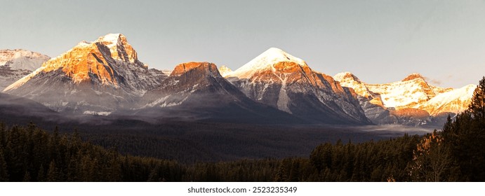 view of the top of a mountain range under the first rays of sunshine in the morning of a clear summer day with low clouds creating a dramatic effect