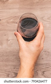 View From The Top Of One Hand Holding A Glass Filled With Red Wine On A Wooden Table