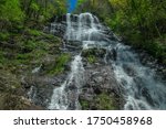 View of the top portion of the Amicalola waterfall in the north Georgia mountains with the strong flow of water rushing over the boulders through the trees alongside on a bright sunny day in spring