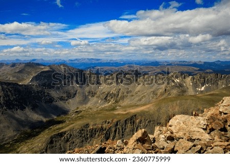 A view from the top of Quandary Peak overlooking the Tenmile Range in the Rocky Mountain, with several clouds overhead.