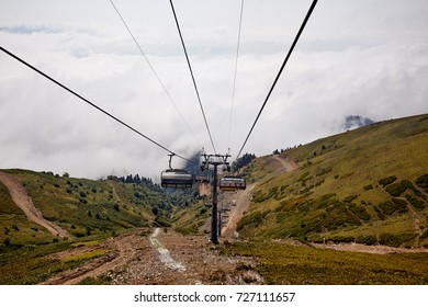 View from top of ropeway with multiple seats and stretched cables above trees in deep fog. Mountains of the North Caucasus.