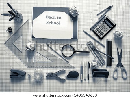 View from the top of scholastic material positioned on a background of squares, visible pencil, a magnifying glass, a compass, two drawing brackets. Back to school concept. Monochrome picture.