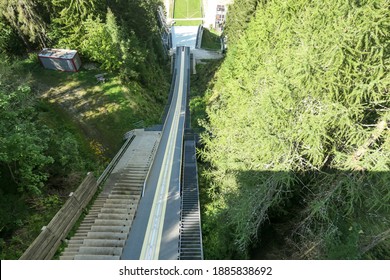 A view from the top of the ski flying hill in Bad Mitterndorf, Austria captured in summer. The ski jump is surrounded by thick forest from each side.