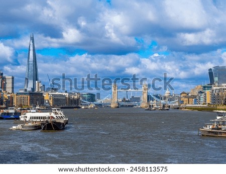 View of Tower Bridge from the River Thames with The Shard skyscraper on the horizon and shipping traffic and tourist ferries sailing along the river on a sunny day in London. United Kingdom.