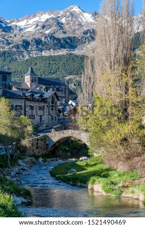 View of the town of Sallent de Gallego (Spain), with the medieval stone bridge over the Gallego River and the snow-capped Pyrenees mountains in the background.